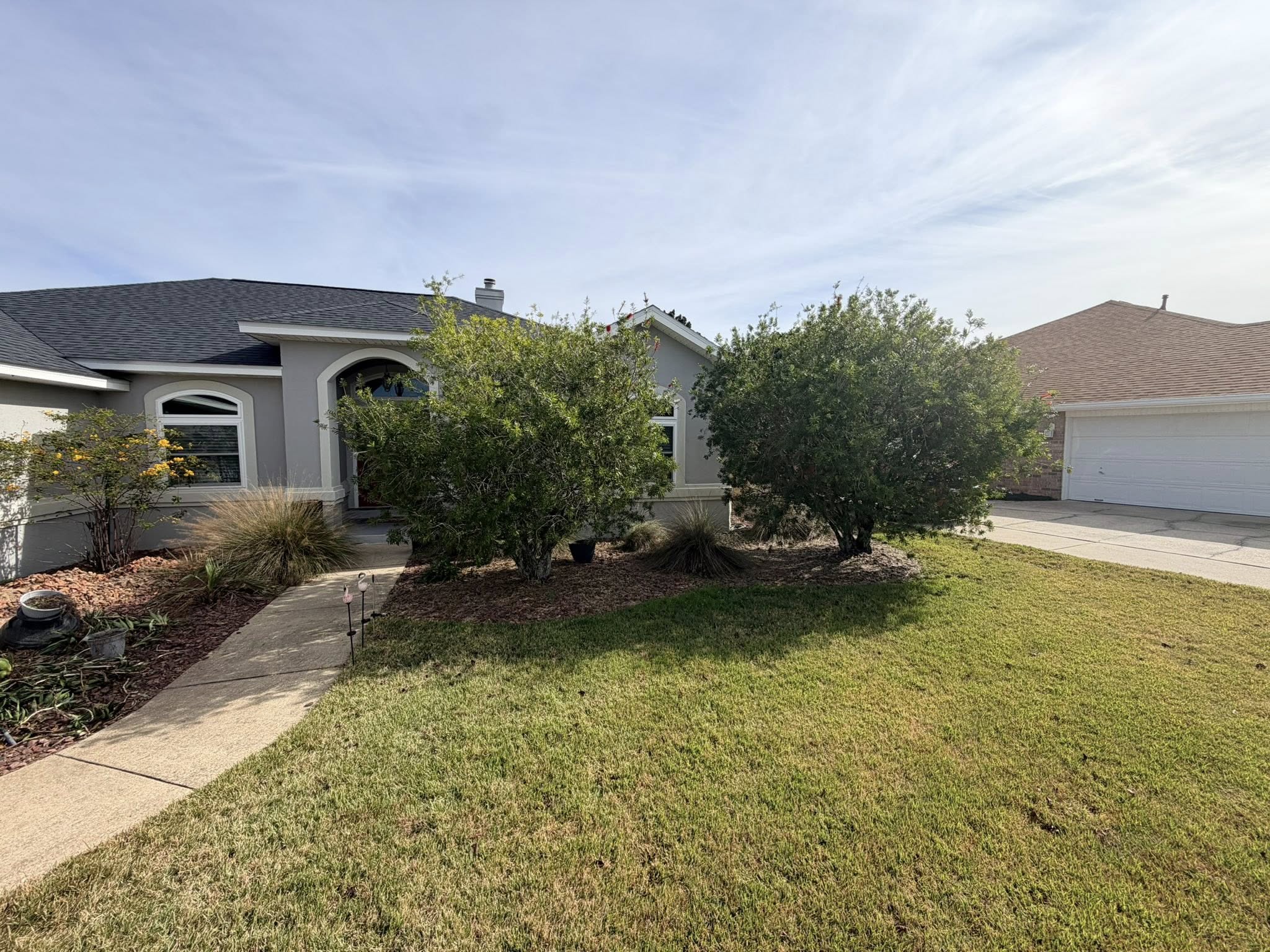 Stucco home with clean curb appeal, trimmed hedges, and fresh mulched beds
